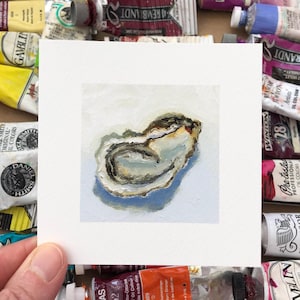 May include: A small square painting of an oyster, rendered in shades of white, gray, and brown, held against a backdrop of colorful paint tubes. The artwork is a detailed depiction of the oyster's form and texture.