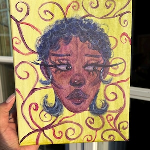 May include: A hand-painted canvas art piece featuring a stylized face with dark skin, blue hair, and a yellow background. The face is painted with purple and red tones, and the background has red swirling vine-like patterns.