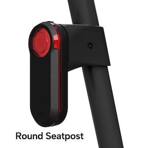 May include: A black bicycle tail light with a circular red lens and a vertical red light strip attached to a round seatpost. The device features a matte black casing and is mounted securely to the frame. The text Round Seatpost is visible.