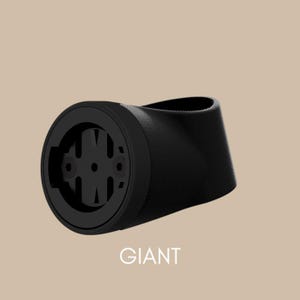 Könnte beinhalten: Schwarze Fahrradcomputerhalterung mit dem Wort "GIANT" in Weiß. Die Halterung besteht aus einem mattschwarzen Material und hat an einem Ende ein kreisförmiges Design mit einer Reihe von Löchern und Rillen.