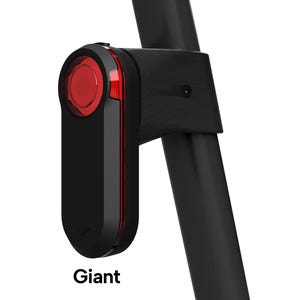 May include: A black bicycle tail light with a circular red lens and a vertical red light strip, mounted on a black seat post. The device features a small, subtle chevron icon at the bottom and the word Giant printed in black text below the unit.