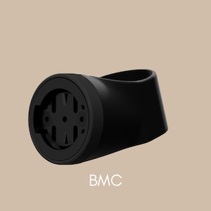 May include: A black bicycle computer mount with a circular front and curved body. The mount has a textured surface and the letters "BMC" are printed in white.