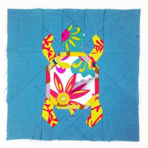 May include: A blue fabric square with a colorful floral patterned turtle design in the center.