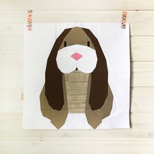 Op de afbeelding: Een bruine en witte papieren patchwork-konijn met lange oren en een roze neus. Het konijn is op een witte achtergrond.