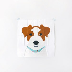May include: A white, brown and black paper pieced dog with a blue and white patterned collar. The dog is looking directly at the viewer.