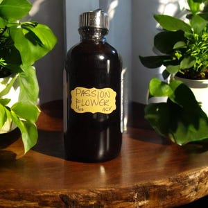 May include: A 4 oz bottle of passion flower infused apple cider vinegar. The bottle has a brown glass body and a silver lid. The label is yellow with black text that reads "Passion Flower ACV".
