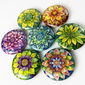 May include: Seven round, colorful, painted ceramic coasters with floral designs. Each coaster features a different flower or floral pattern, including a purple flower, a green and blue flower, a yellow flower, a red and yellow flower, and a green and yellow flower.