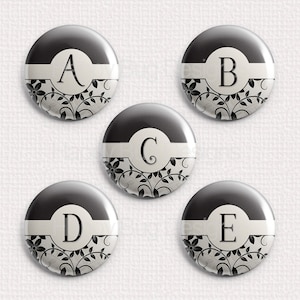 May include: Five black and white round buttons with a white background and black floral design. Each button features a white letter, A, B, C, D, and E.