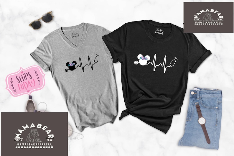 May include: Two grey and black t-shirts with a Mickey Mouse design and a heartbeat graphic. The graphic includes a stethoscope and a flower crown on Mickey Mouse's head. The text on the shirts reads "Ships Today".