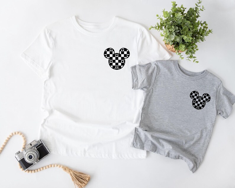 May include: Two t-shirts, one white and one gray, with a black and white checkered Mickey Mouse head design on the front.