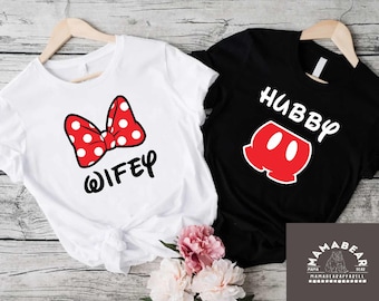 May include: Two white t-shirts with a red and white bow and the word "WIFEY" on one shirt and the word "HUBBY" and a red Mickey Mouse-style silhouette on the other shirt.