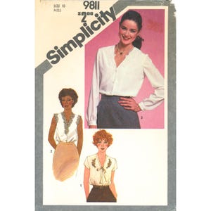 May include: A Simplicity sewing pattern envelope, number 9811, size 10, featuring illustrations and a photograph of three variations of a blouse. The designs include long sleeves with lace trim, sleeveless with lace trim, and short sleeves with embroidery.