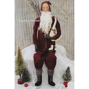 Puede incluir: Un muñeco de Papá Noel de fieltro hecho a mano que lleva un traje rojo y sostiene un ganso blanco. El muñeco está sentado sobre una superficie blanca con dos pequeños árboles de Navidad verdes en el fondo. El texto "Country Harvest" es visible en la imagen.