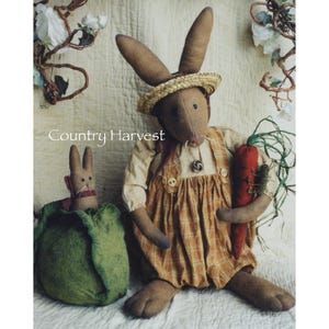 May include: Two handmade fabric bunny dolls. The larger bunny is wearing a straw hat, overalls, and holding a carrot. The smaller bunny is inside a green cabbage.