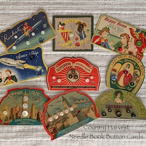 May include: A collection of vintage needle book button cards with various designs. The cards feature illustrations of rockets, spaceships, women, and cityscapes. Each card holds an assortment of buttons. The text on the cards includes "Rocket", "Space Ship", and "Empire State".