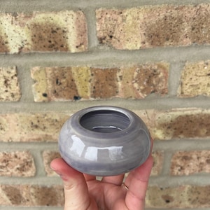 May include: A small, round, ceramic bowl with a light purple glaze. The bowl has a smooth, glossy finish and a slightly rounded lip.