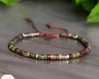 May include: A multi-colored beaded bracelet with a red string closure. The beads are a mix of green, brown, and red.