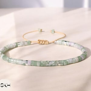 Puede incluir: Un brazalete de cuentas verdes y blancas con cierre de nudo deslizante. El brazalete está hecho con cuentas pequeñas de forma cuadrada y tiene un diseño simple y minimalista.