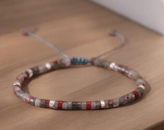 May include: A gray, red, and silver beaded bracelet with a sliding knot closure.