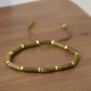 May include: A green stone beaded bracelet with gold accents. The bracelet is adjustable with a sliding knot.