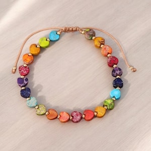 Op de afbeelding: Een regenboogkleurig armband met hartvormige kralen en een bruine koordsluiting.
