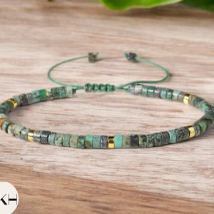 Puede incluir: Un brazalete de cuentas verdes y doradas con cierre de nudo deslizante. El brazalete está hecho de pequeñas cuentas redondas con un esquema de color verde y dorado.