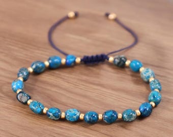 Puede incluir: Un brazalete de cuentas azules y doradas con cierre de cordón azul. Las cuentas son de forma ovalada y tienen un patrón de mármol.