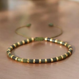 Pode incluir: Uma pulseira minimalista com contas alternadas verdes e douradas. A pulseira é enfiada em um cordão verde e possui um fecho ajustável. As pequenas contas redondas criam um design simples e elegante.