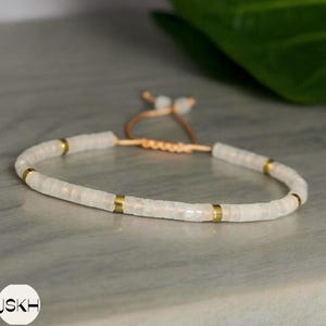 May include: A white beaded bracelet with gold accents and a brown leather cord closure.