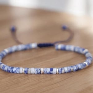 May include: A blue and silver beaded bracelet with a sliding knot closure. The beads are small and round, and the bracelet is adjustable.