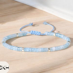 以下が含まれることがあります： 薄い青色のビーズブレスレット。シルバーのアクセントと青い紐の留め具が付いている。