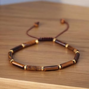 Könnte beinhalten: Ein braunes und goldenes Perlenarmband mit einem verschiebbaren Knotenverschluss. Die Perlen sind aus Tigerauge-Stein und haben einen goldenen Akzent.