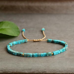 Peut inclure: Un bracelet en perles bleu turquoise avec un fermoir coulissant doré réglable. Le bracelet est composé de petites perles carrées et est enfilé sur un cordon fin doré.