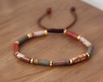 May include: A multi-colored beaded bracelet with brown, red, and white beads. The beads are separated by gold spacers. The bracelet is tied with a brown cord.