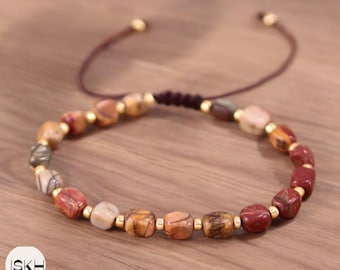May include: A brown and red beaded bracelet with gold accents. The bracelet is made of natural stones and has a sliding knot closure.