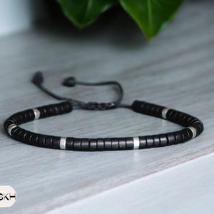 Puede incluir: Un brazalete de cuentas negras con detalles plateados y cierre de cordón negro.
