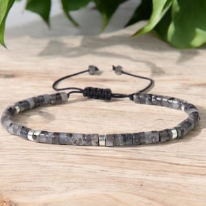 以下が含まれることがあります： グレーのビーズブレスレットにシルバーのアクセントと調節可能なブラックコードが付いている。