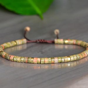 Puede incluir: Un brazalete de cuentas verdes, rosas y doradas con cierre de cordón marrón.