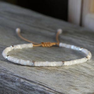May include: A white beaded bracelet with silver accents and a brown leather cord closure.