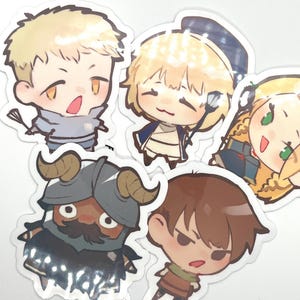 Peut inclure: Plusieurs autocollants de personnages de dessins animés. Les autocollants présentent divers personnages, dont un avec un casque à cornes et d'autres avec des tenues et des expressions variées. Les autocollants sont colorés et ont une finition brillante.