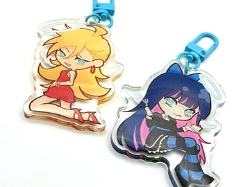 Könnte beinhalten: Zwei Schlüsselanhänger aus Acryl mit Anime-Engelsfiguren. Ein Schlüsselanhänger zeigt eine blonde Figur in einem roten Kleid, der andere eine Figur mit blauen Haaren und einem schwarzen Outfit. Beide haben blaue Verschlüsse.