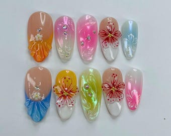 May include: Ten fake nails with different designs. Some nails have a gradient effect, others have a flower design, and some have a 3D design. The nails are all oval shaped and have a glossy finish.