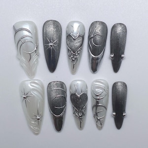 May include: Ten false fingernails with different silver and white designs. The designs include hearts, stars, and swirls.