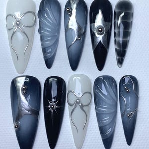 Puede incluir: Diez uñas postizas largas en forma de almendra con diferentes diseños. Los diseños incluyen un lazo plateado, una estrella plateada, un remolino plateado y un patrón geométrico plateado. Las uñas están pintadas en tonos de blanco, negro y gris.