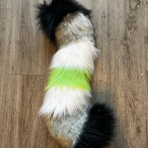 May include: A long, plush faux fur tail featuring a color-blocked design. The tail transitions from a solid black tip to a mottled gray and brown section, followed by a band of white, a vibrant lime green stripe, another white band, and a black base.