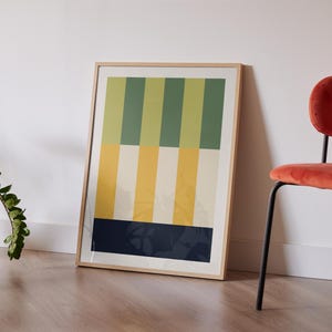 May include: A framed abstract print with vertical stripes in shades of green, yellow, and white. The bottom stripe is a dark blue color. The frame is a light wood color.