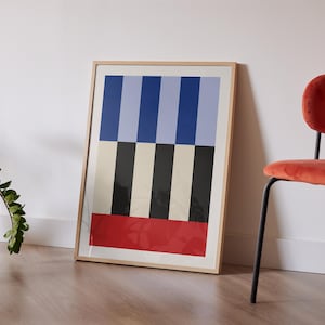 May include: A framed abstract print with a geometric pattern of blue, white, black, and red stripes. The print is hanging on a white wall next to a red velvet chair.