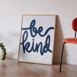 May include: A framed print with a white background and the words "be kind" written in blue cursive.