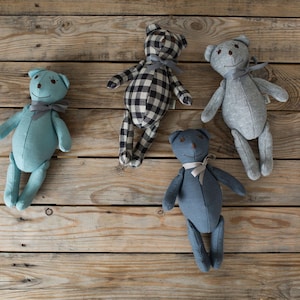 Puede incluir: Cuatro osos de peluche en diferentes colores y patrones. Un oso azul, un oso gris, un oso a cuadros blanco y negro y un oso azul oscuro.