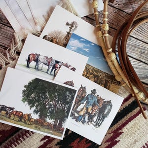 May include: A collection of art prints featuring Western themes. The prints depict scenes of cowboys, horses, and landscapes, including a windmill and a herd of cattle. A leather rope and a decorative rope are also visible.